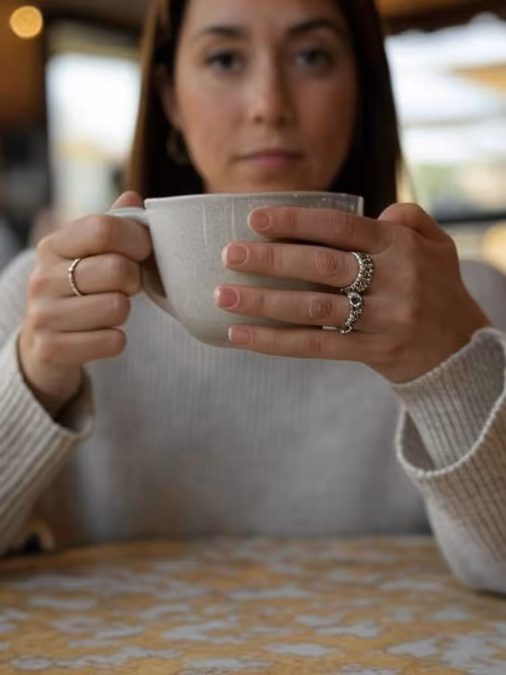 Close-up of a woman's hands holding a coffee cup during a thoughtful moment, expensive jewelry visib
