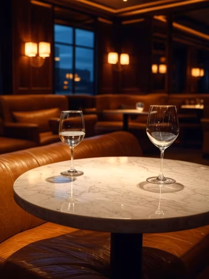 Intimate upscale lounge setting with leather seats and dim ambient lighting, two wine glasses on mar