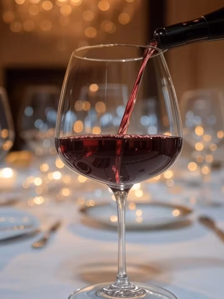 Red wine being poured into crystal glass at elegant dinner table, close-up shot, bokeh lights in bac